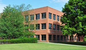 Outside view of a red-brick building with the words Technology Support Building on one wall with trees in the foreground.